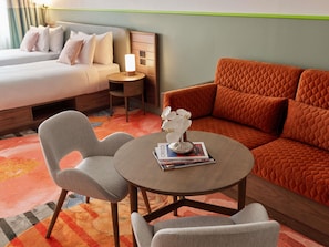 Une chambre d’hôtel comprenant un lit, un canapé, deux fauteuils, une petite table avec une lampe et un vase décoratif.