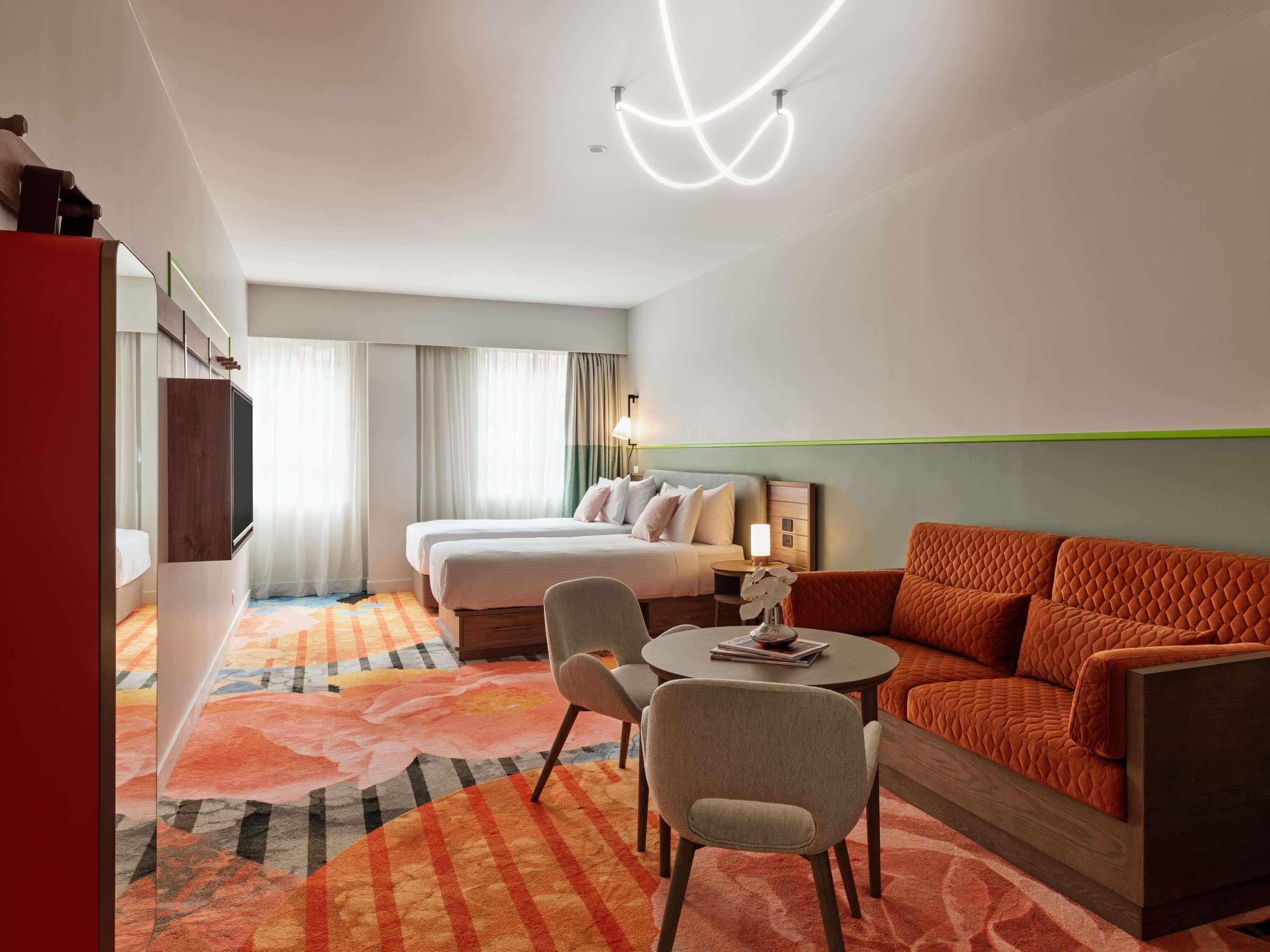 A hotel room with a bed, a sofa, a chair, a small table, and a TV.