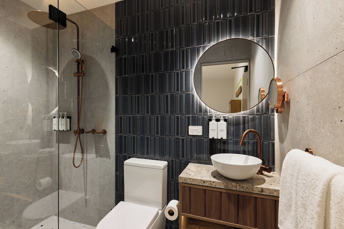 Une salle de bain moderne avec une douche à parois de verre, des toilettes, un lavabo avec un miroir rond et un porte-serviettes.