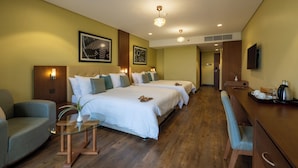 A hotel room with three beds, a sitting area, a desk with a chair, and a television.