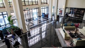 Un vestíbulo amplio con techo alto, ventanas grandes y una zona de estar central con sofás y una mesa de centro.