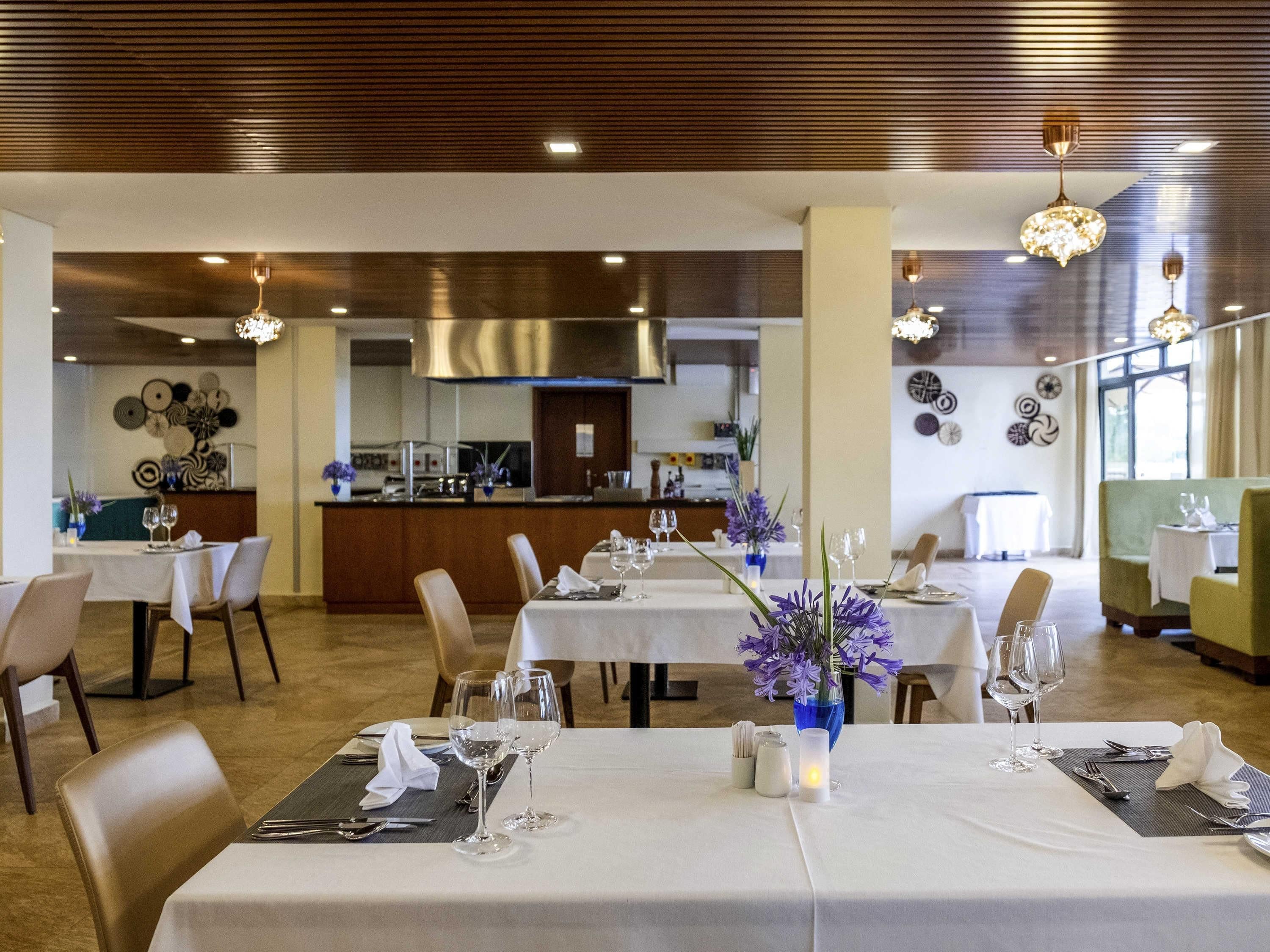 A restaurant with tables set for dining, a kitchen in the background, and decorative wall art.