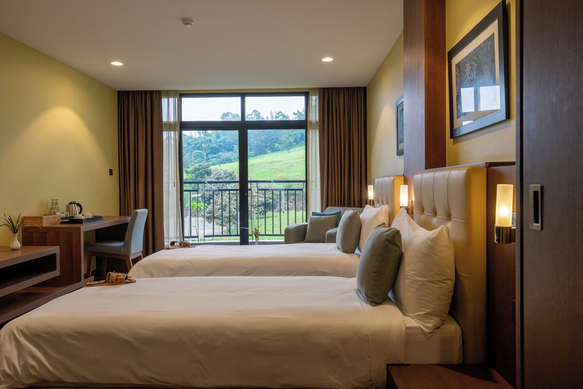 Une chambre d’hôtel avec deux lits, un bureau et une vue sur un paysage verdoyant.