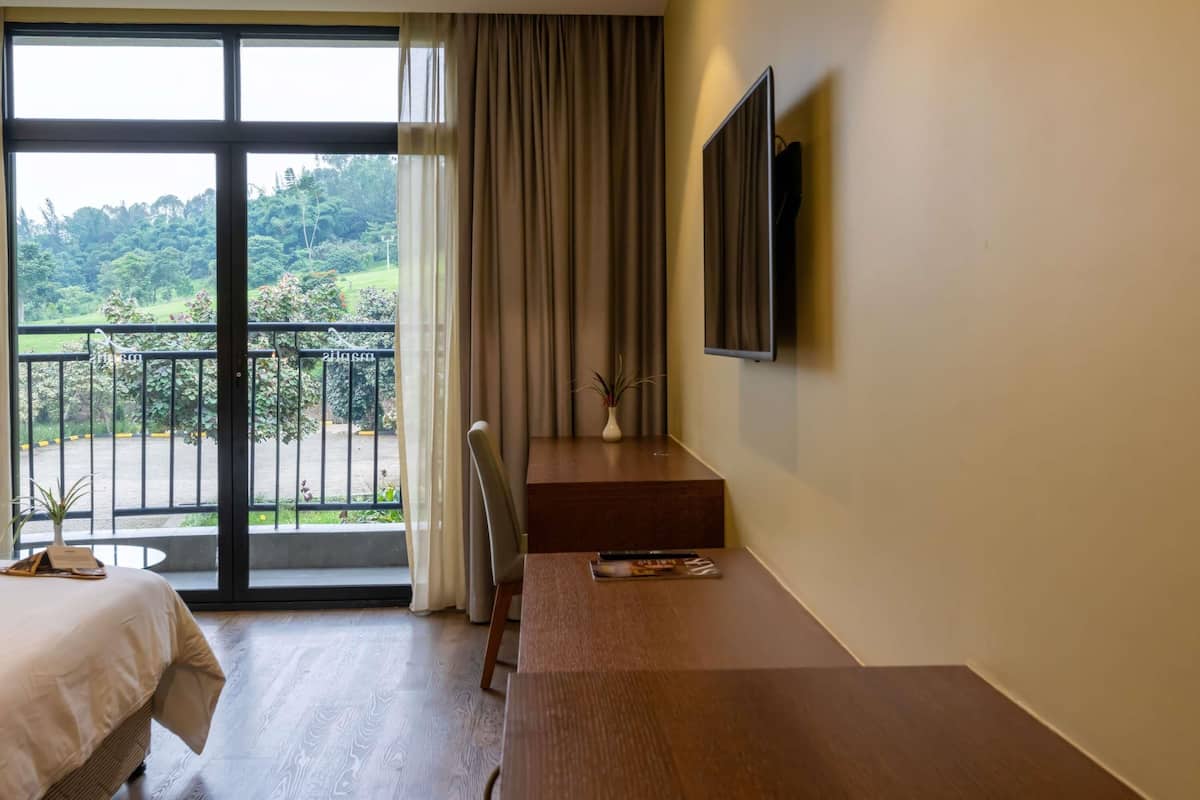 Quarto de hotel com cama, escrivaninha, cadeira, televisão e varanda com vista para vegetação.