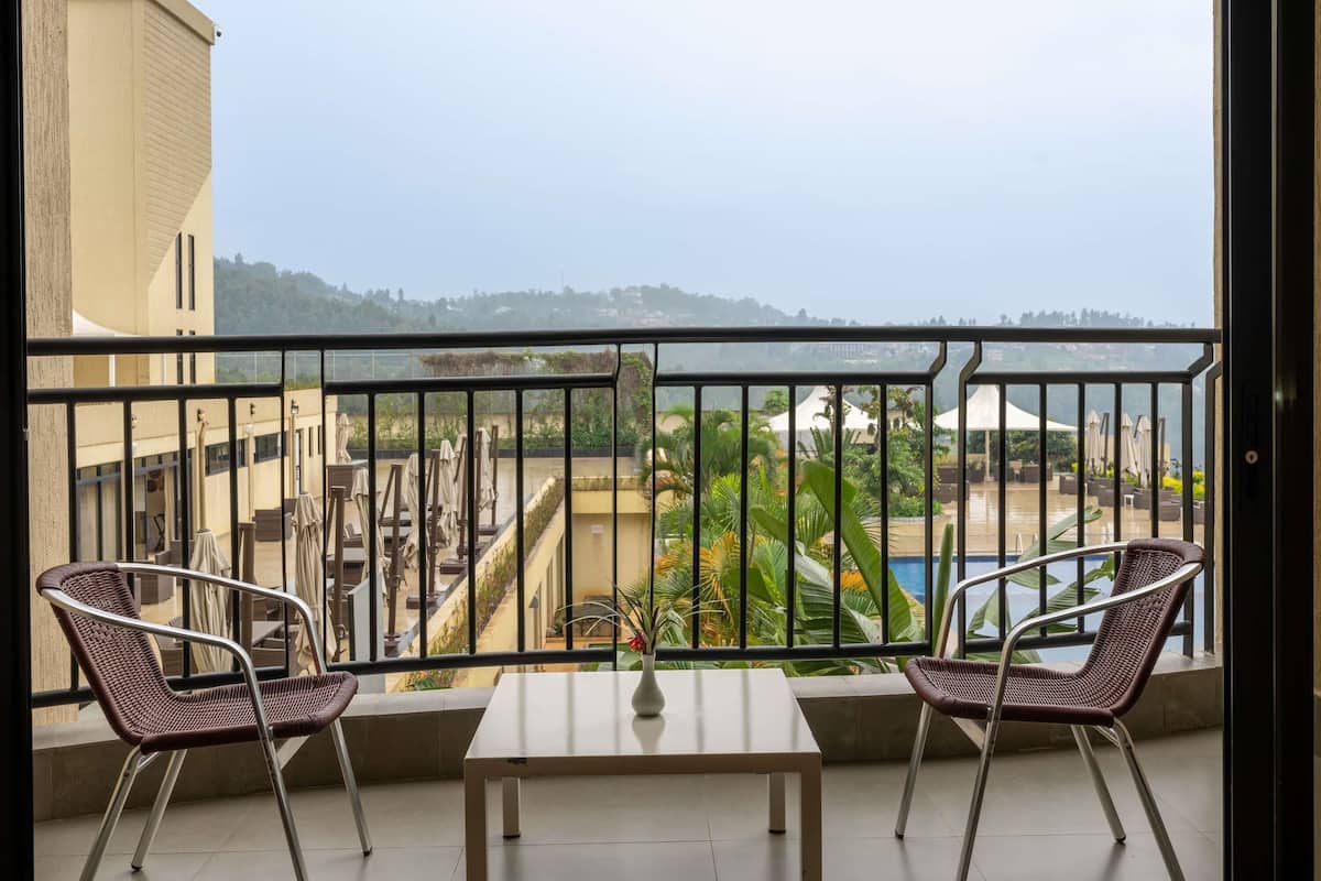 Varanda com duas cadeiras de vime e uma mesa, com vista para uma piscina e vegetação.