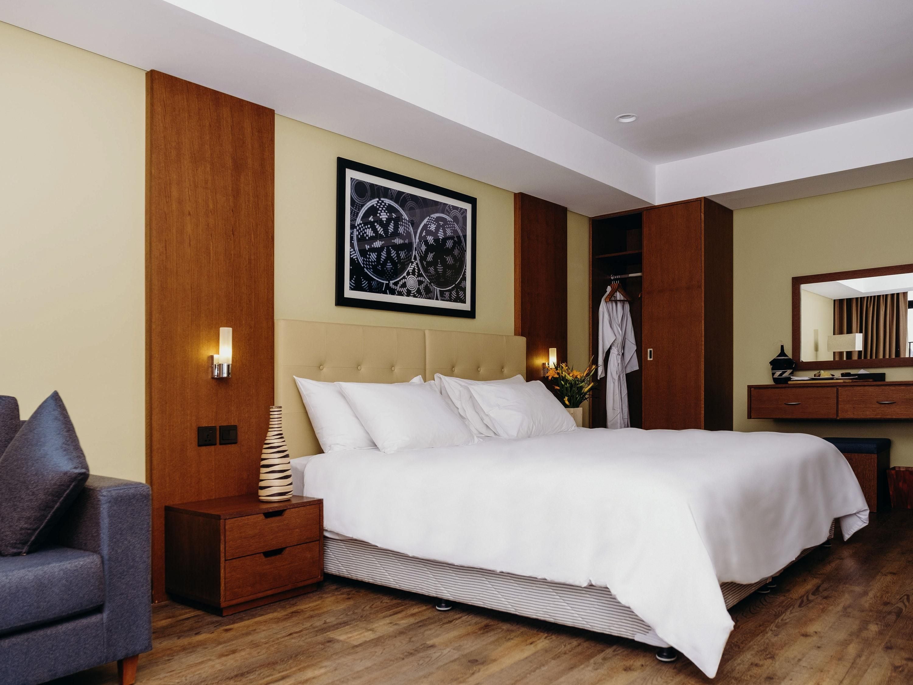 Una habitación de hotel con una cama grande, una mesita de noche, una lámpara, una silla, un armario y un espejo.