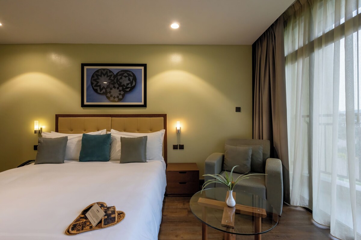Une chambre d’hôtel comprenant un lit, un canapé, une table en verre avec un vase et une œuvre d’art murale.