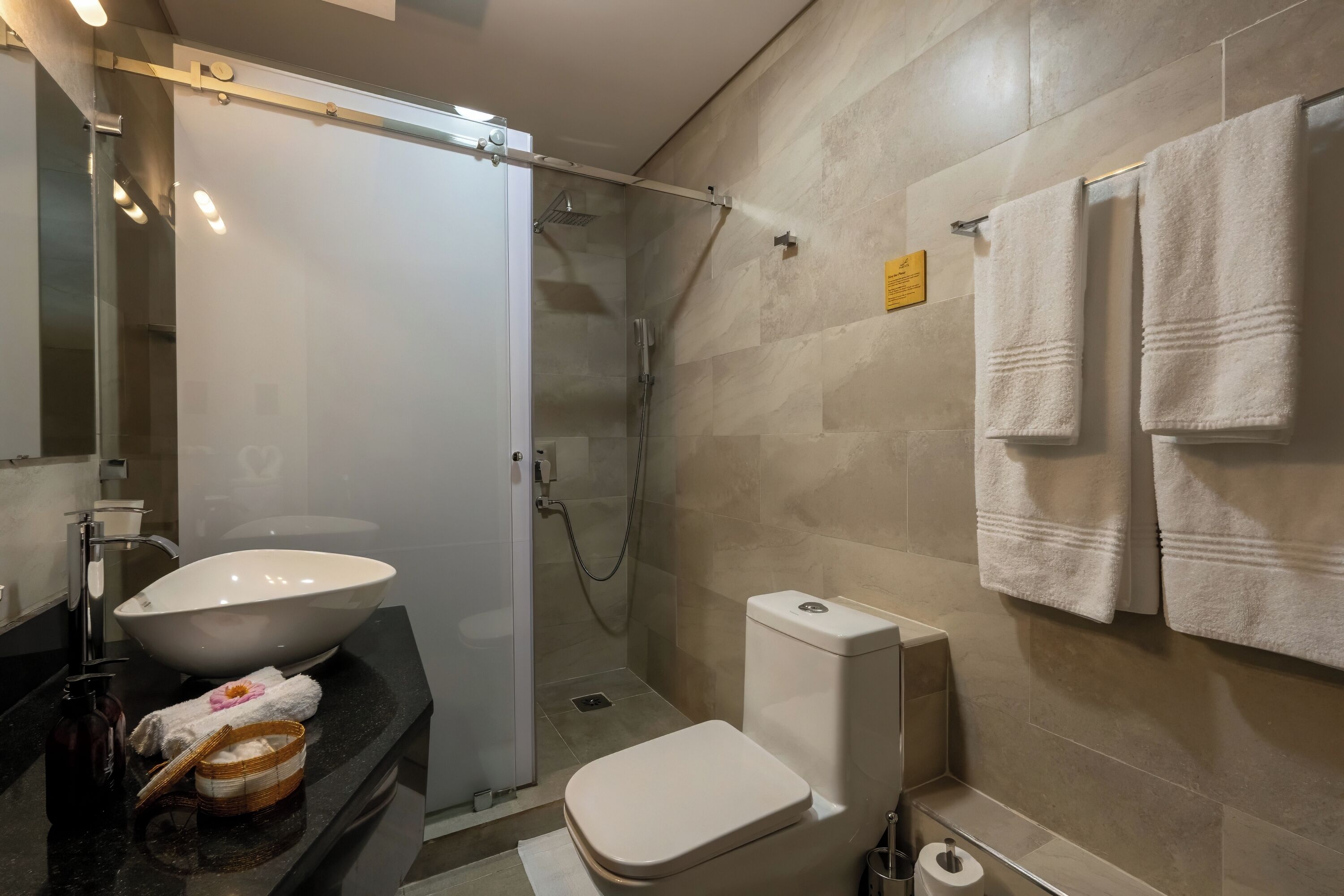 Un bany modern amb un gran lavabo blanc, un vàter i una dutxa amb envà.