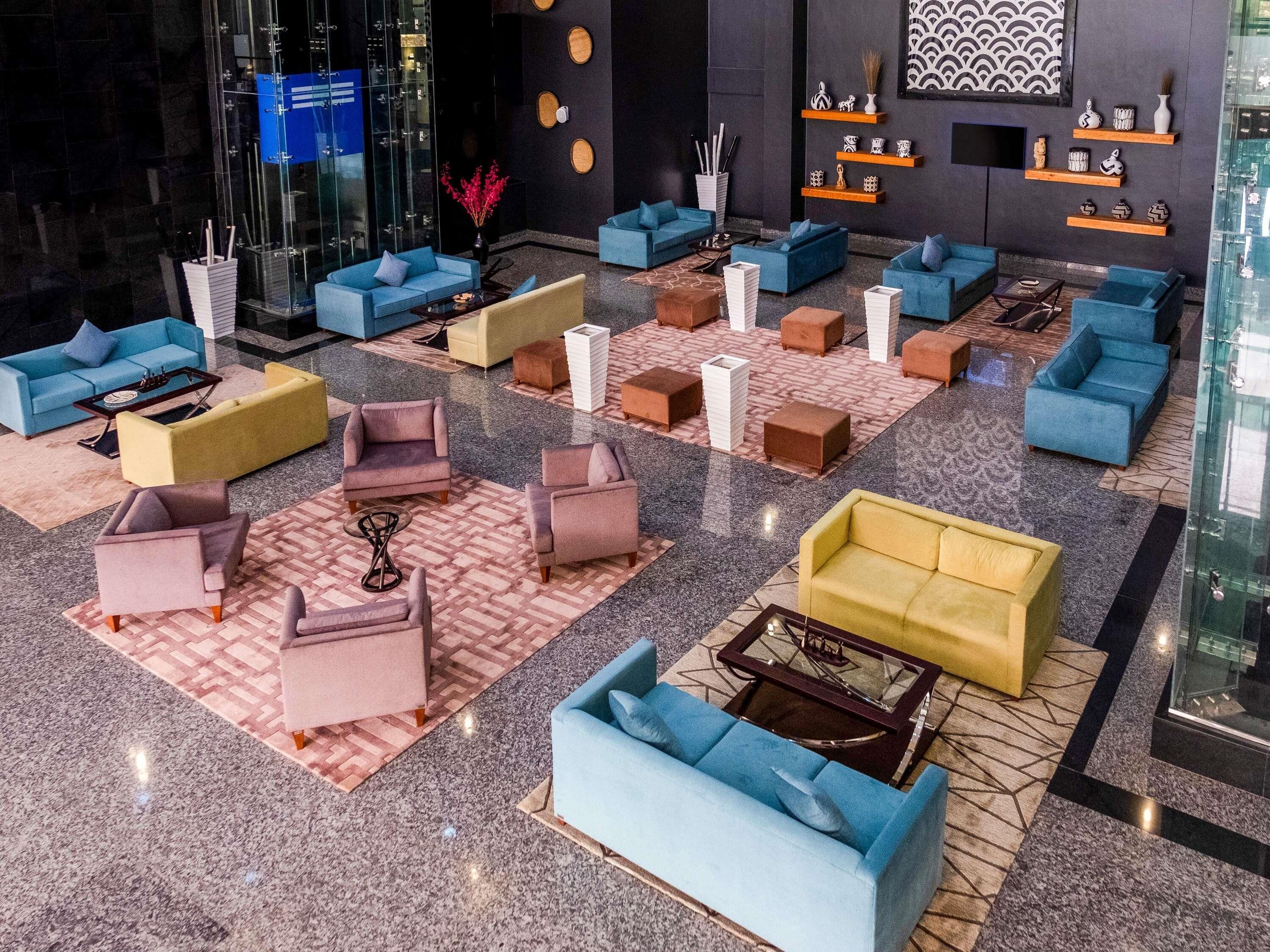 A modern lobby with multiple seating areas, including sofas and armchairs, arranged on patterned carpets.