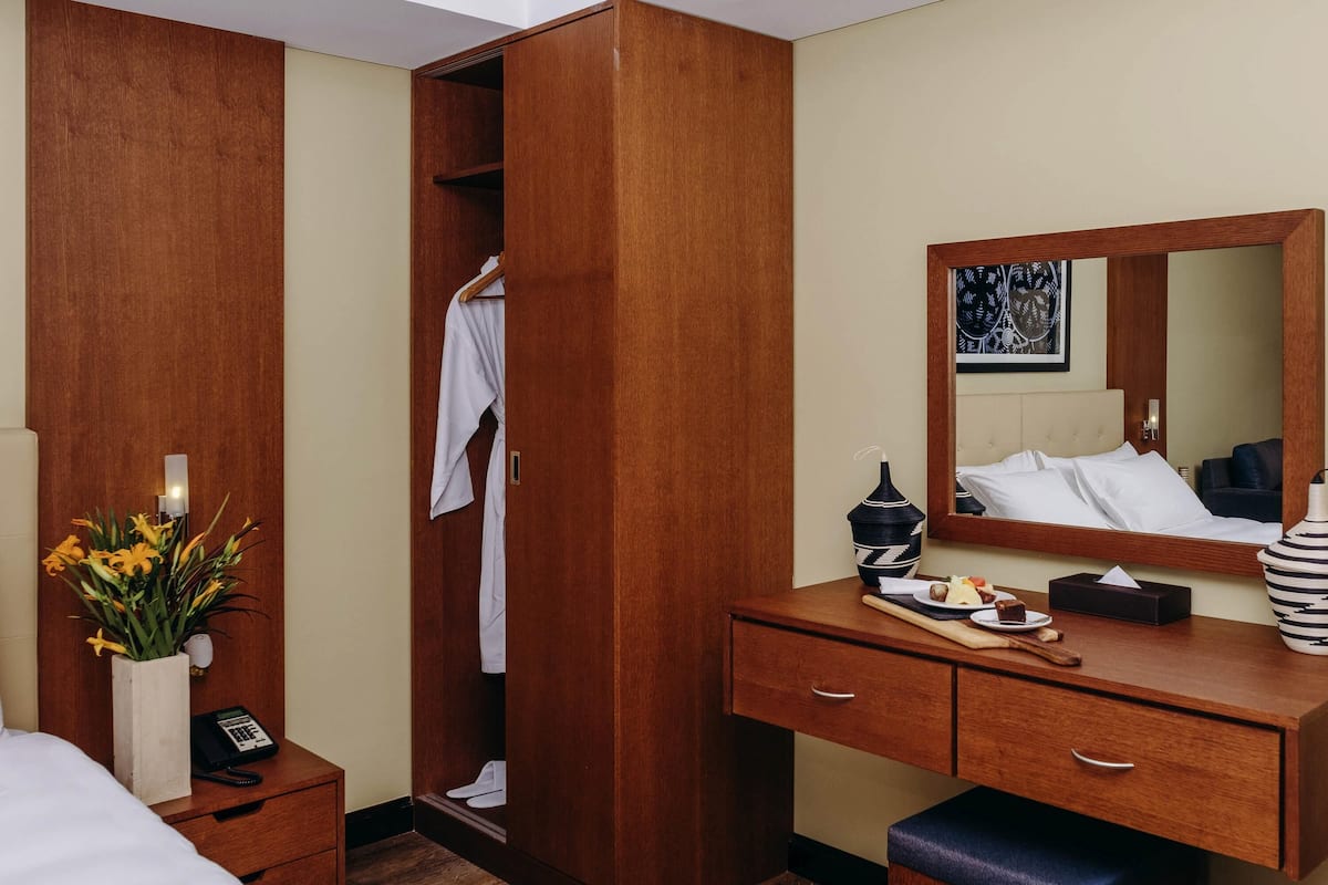 A hotel room with a wooden wardrobe, a bedside table with a vase of flowers, a mirror, and a bed.