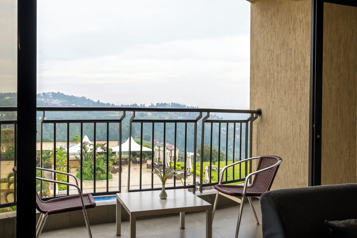Un balcon avec vue sur un lac et des collines, comprenant deux fauteuils en osier et une petite table.