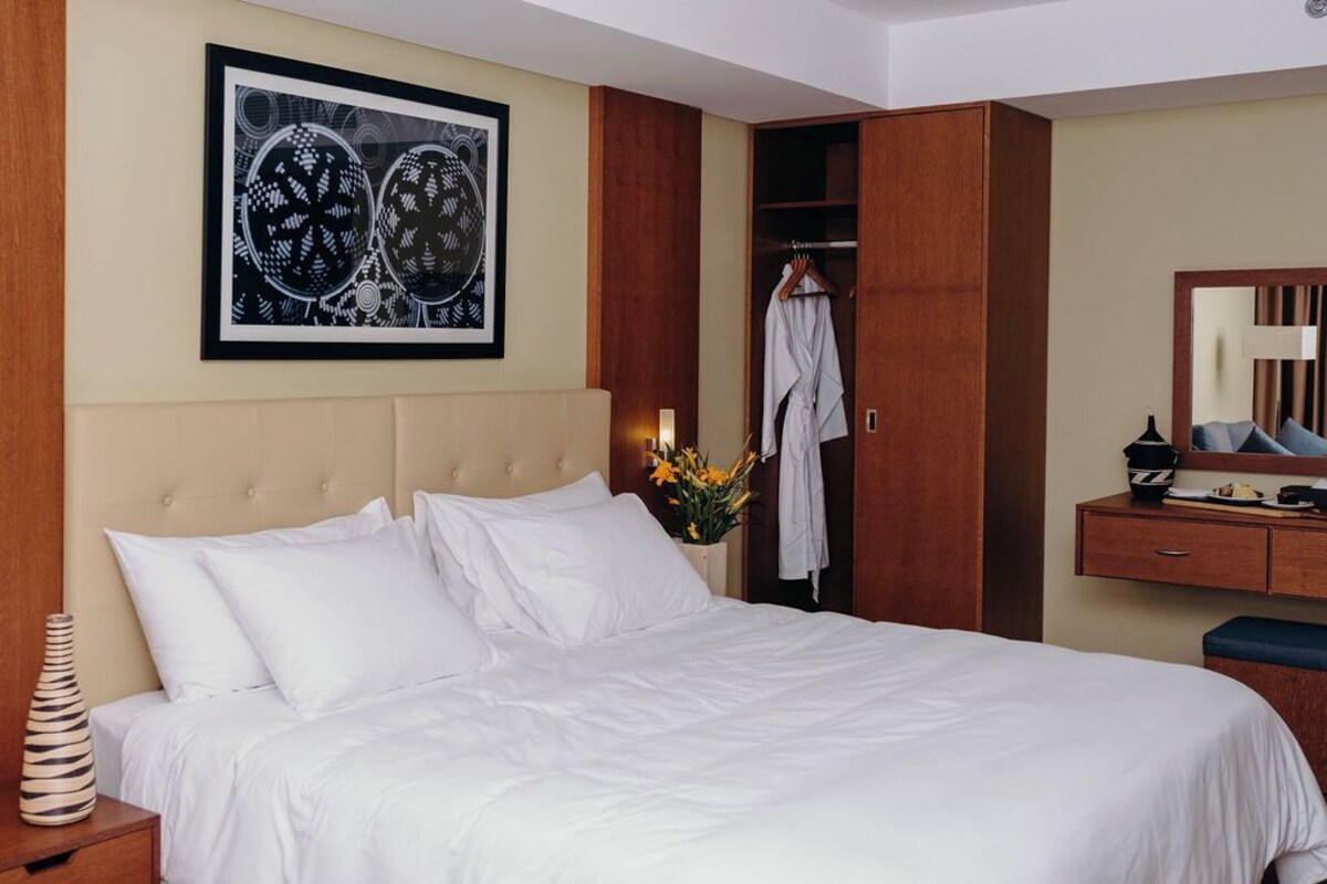 Une chambre d’hôtel avec un lit, une armoire, un miroir et une œuvre d’art encadrée accrochée au mur.