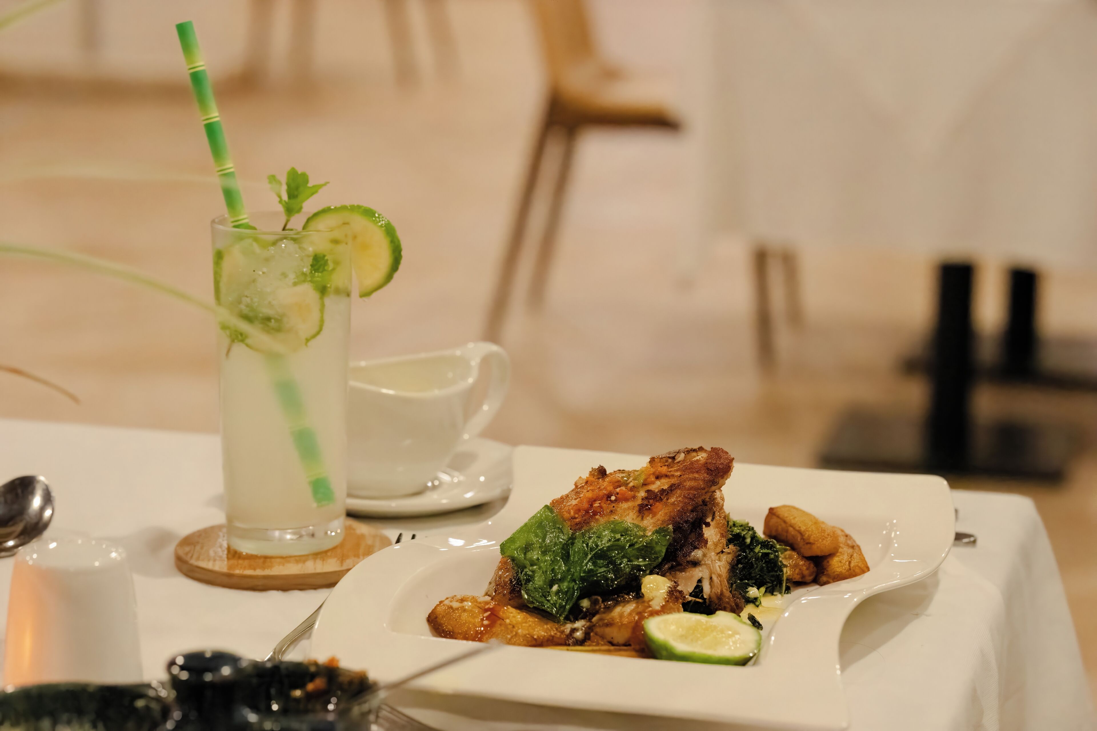 A dining table with a plate of food, a glass of beverage with a straw, and a small cup.