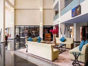 Un hall d’entrée spacieux avec un plafond haut, un comptoir de réception et un espace détente avec des canapés et une table basse.