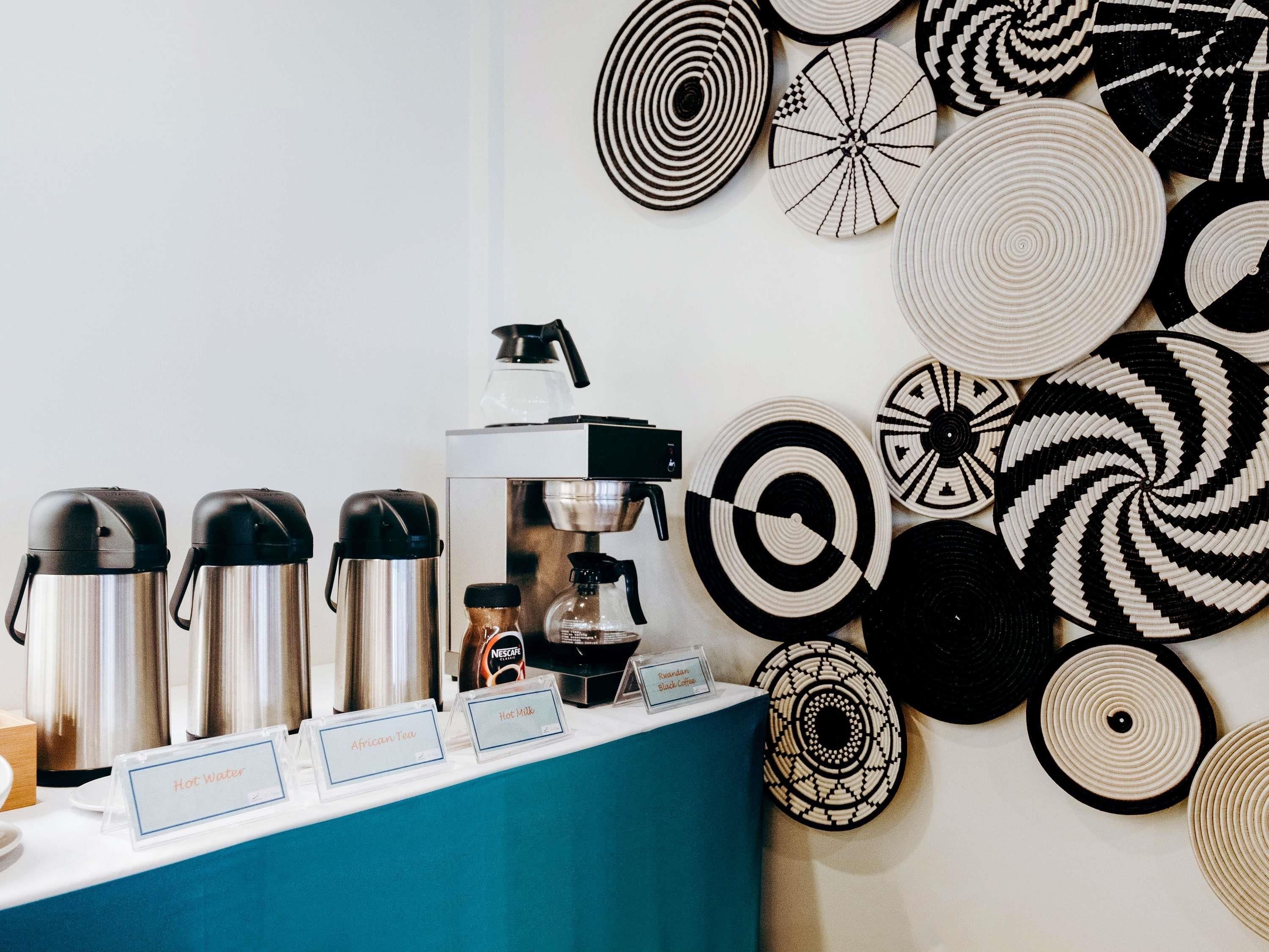 En kaffestation med kaffemaskine, termokrus og en væg med cirkulære mønstre.