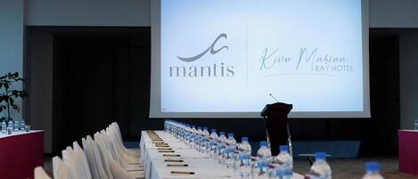 Un salón de conferencias con una larga mesa dispuesta para una reunión, un atril y una pantalla mostrando el logotipo y el nombre del Hotel Kiwa Marina.
