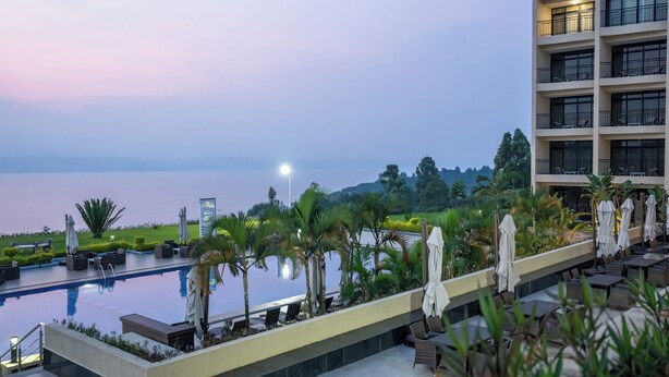 Zona junto a la piscina con vista al mar, mobiliario exterior y un edificio con balcones.