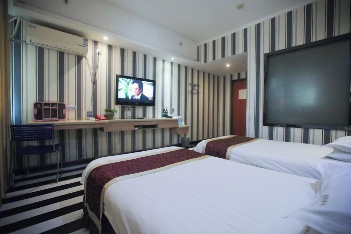 A hotel room with two beds, a TV, a desk, and a striped wall.