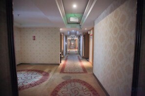 A hotel corridor with patterned carpet, a ceiling light, and a fire alarm on the wall. - Yining V8 Business Hotel (Teachers University) (Yining City)