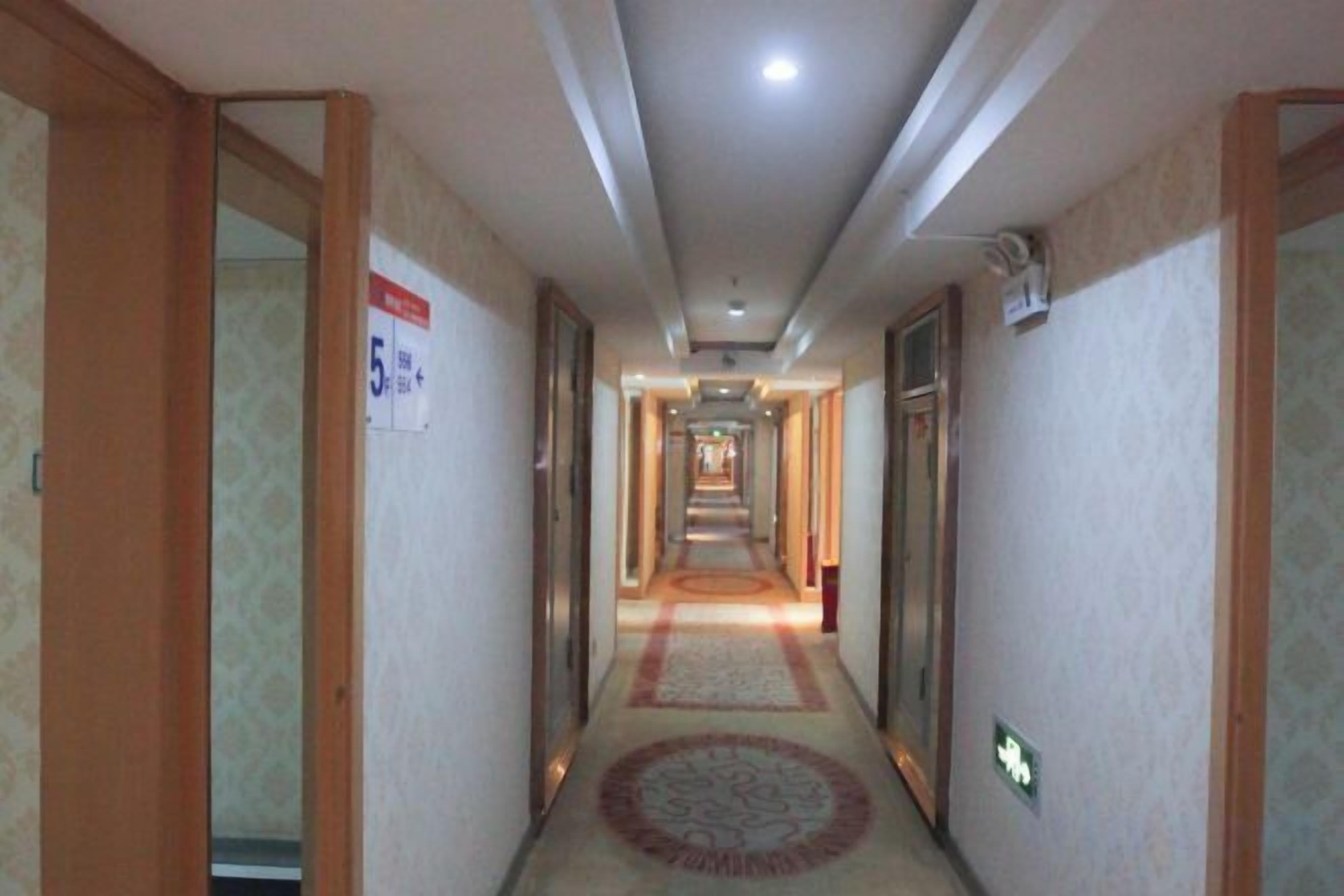 A hotel hallway with carpeted floors, doors on both sides, and a sign indicating room number 5.