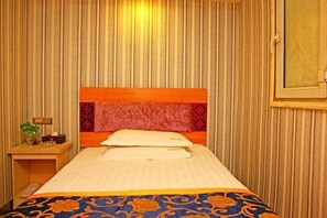 A hotel room with a striped wallpaper, a bed with a patterned bedspread, a nightstand with a lamp, and a window with a view. - Yining V8 Business Hotel (Teachers University) (Yining City)