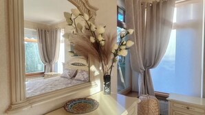 Un dormitorio con un espejo grande, un aparador, una silla y una ventana con cortinas.