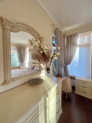 A bedroom with a large mirror, a dresser, a chair, and a window with curtains. - Elegant Apartment Near Bulduri Beach (Jūrmala)