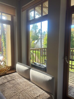 A room with a large window, a cushioned bench, and a view of a wooden deck and trees. - Elegant Apartment Near Bulduri Beach (Jūrmala)