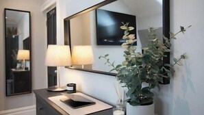 A bathroom with a large mirror, two wall-mounted lamps, a sink with a white countertop, a small potted plant, and a framed picture on the wall. - King Suite close to Manchester City Centre, R3 (Stockport)