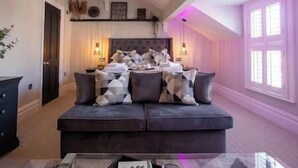 A living room with a dark-colored sofa, a coffee table, and a fireplace. - King Suite close to Manchester City Centre, R3 (Stockport)