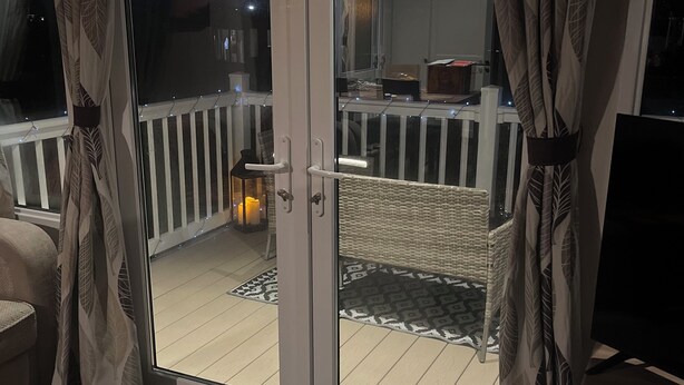 A balcony with a white railing, a wicker chair, a lantern, and a patterned rug. - Tranquil Waterside Lodge in Tunstall (Hull)