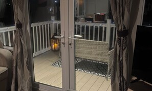 A balcony with a white railing, a wicker chair, a lantern, and a patterned rug. - Tranquil Waterside Lodge in Tunstall (Hull)