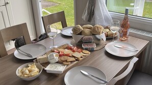 A dining table set with various cheeses, crackers, and bread, along with wine glasses and a bottle of rosé wine. - Tranquil Waterside Lodge in Tunstall (Hull)