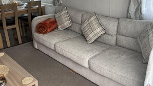 A cozy living area with a sofa, a wooden table, and a dining table. - Tranquil Waterside Lodge in Tunstall (Hull)