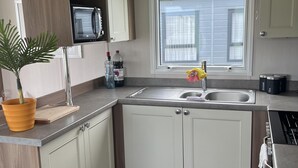 A kitchen with a double sink, a microwave, and a window. - Tranquil Waterside Lodge in Tunstall (Hull)