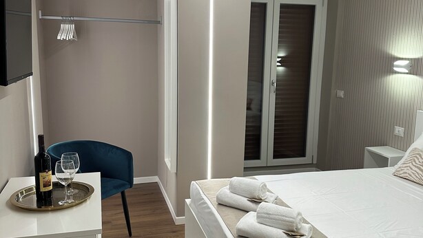 A modern hotel room with a neatly made bed, a bedside table with a bottle and glasses, a chair, and a wardrobe. - Luxurious apartment, close to the center (Roma)
