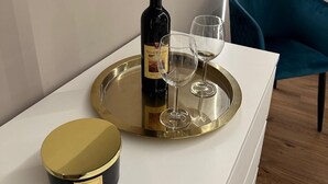A modern living room with a flat-screen TV mounted on the wall, a blue chair, and a white console table with a tray holding a bottle of wine and two glasses. - Luxurious apartment, close to the center (Roma)