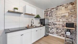 A kitchen with white cabinets, a black refrigerator, a brick wall, and a shelf with plants. - Cozy studio in awesome Fort Lauderdale with WiFi and parking (Fort Lauderdale)