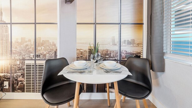 A dining area with a table set for two, large windows with a cityscape view, and black chairs. - Cozy studio in awesome Fort Lauderdale with WiFi and parking (Fort Lauderdale)