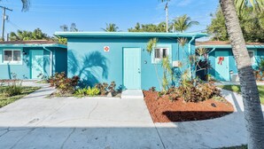A row of turquoise single-story buildings with a central door, surrounded by small plants and palm trees. - Cozy studio in awesome Fort Lauderdale with WiFi and parking (Fort Lauderdale)