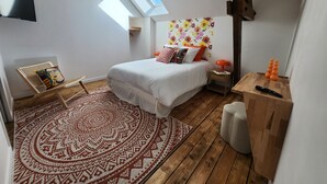 A bedroom with a bed, a chair, a desk, a TV, and a window. - Chambre Frida Kalho (Laval)