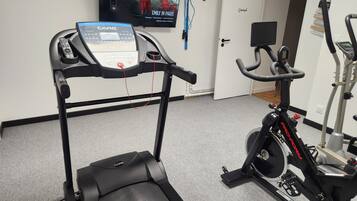 Une salle de sport à domicile équipée d’un tapis de course, d’un vélo d’appartement et d’un téléviseur diffusant un film.