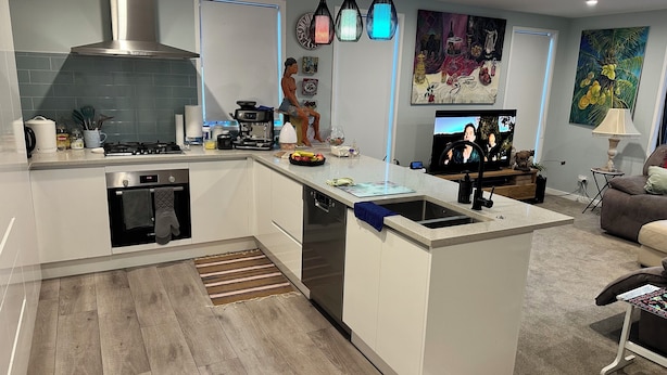 Eine moderne Küche mit Kochinsel, Backofen und Geschirrspüler. Es gibt einen Essbereich mit Tisch und Stühlen sowie ein Wohnzimmer mit Fernseher und Sitzgelegenheiten.