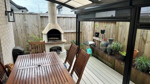 Eine Terrasse im Freien mit einem aus Stein gebauten Pizzaofen, einem Holztisch und Stühlen.