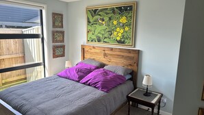 Ein Schlafzimmer mit einem Bett, violett-grauen Bettwäsche, einem hölzernen Kopfteil, einem Nachttisch mit Lampe und einem großen gerahmten Gemälde über dem Bett.