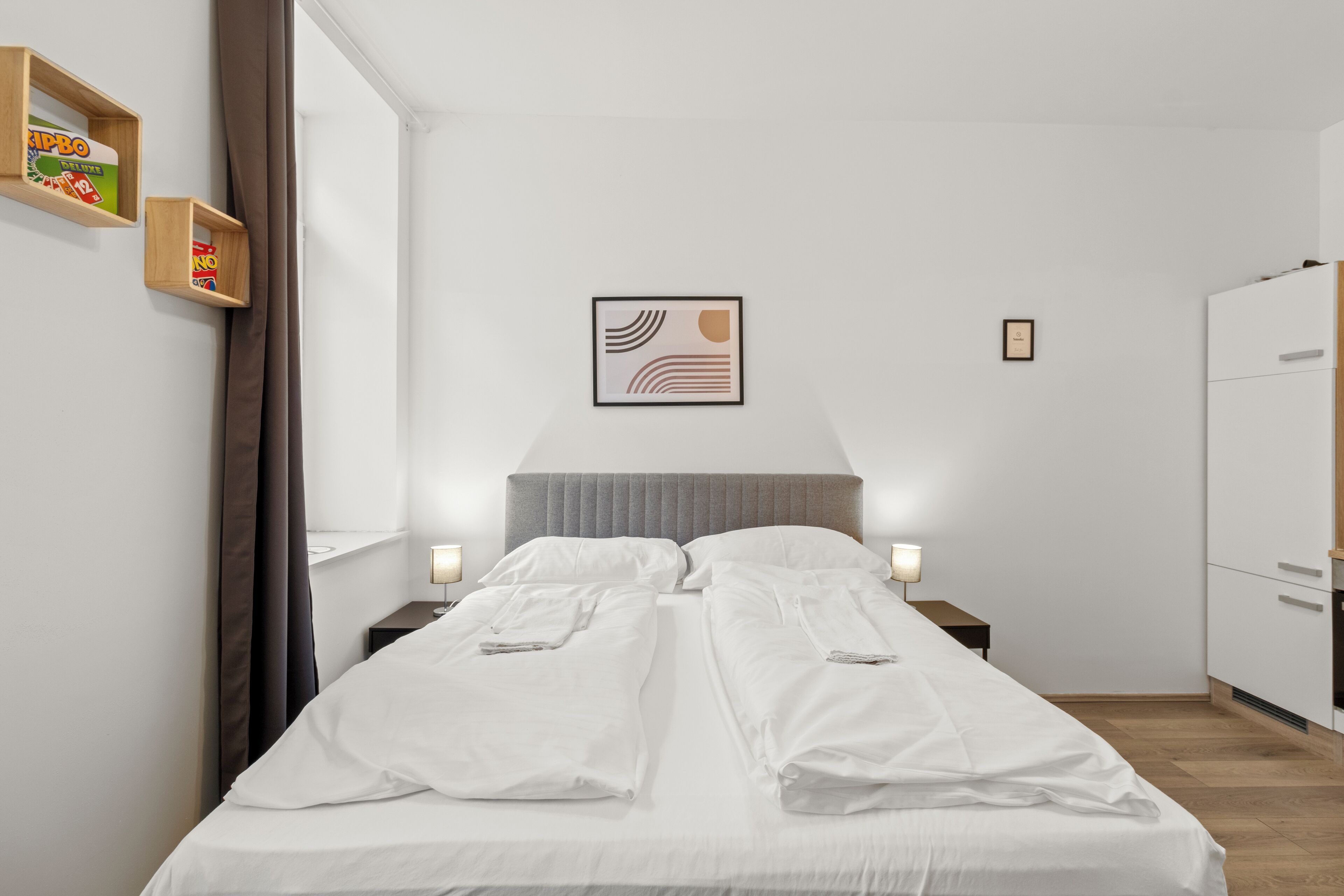 Una habitación de hotel con cama, mesitas de noche, un armario y una obra de arte enmarcada en la pared.