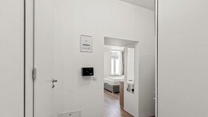 Un pasillo con una puerta, un detector de humo y una pequeña rejilla.