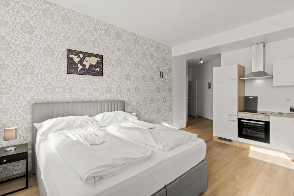 Un dormitorio moderno con una cama bien tendida, un mapa del mundo en la pared y una zona de cocina con armarios blancos y una estufa.