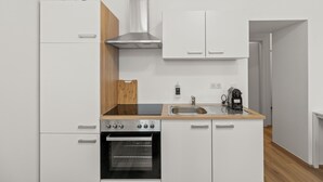 Una cocina moderna con armarios blancos, una campana extractora de acero inoxidable, un horno empotrado y una cafetera en la encimera.