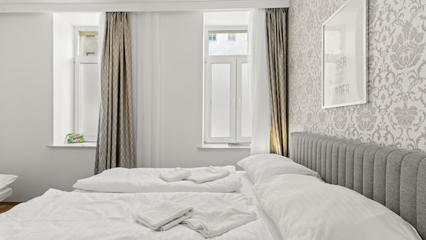 Habitación de hotel con una cama grande, una ventana con cortinas, un radiador y un cuadro en la pared.